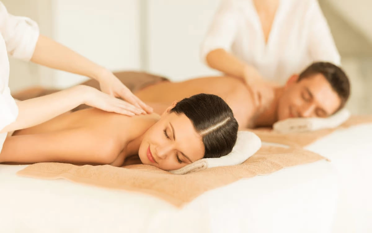 A couple both receiving a massage treatment. They are both lying face down, looking very relaxed.