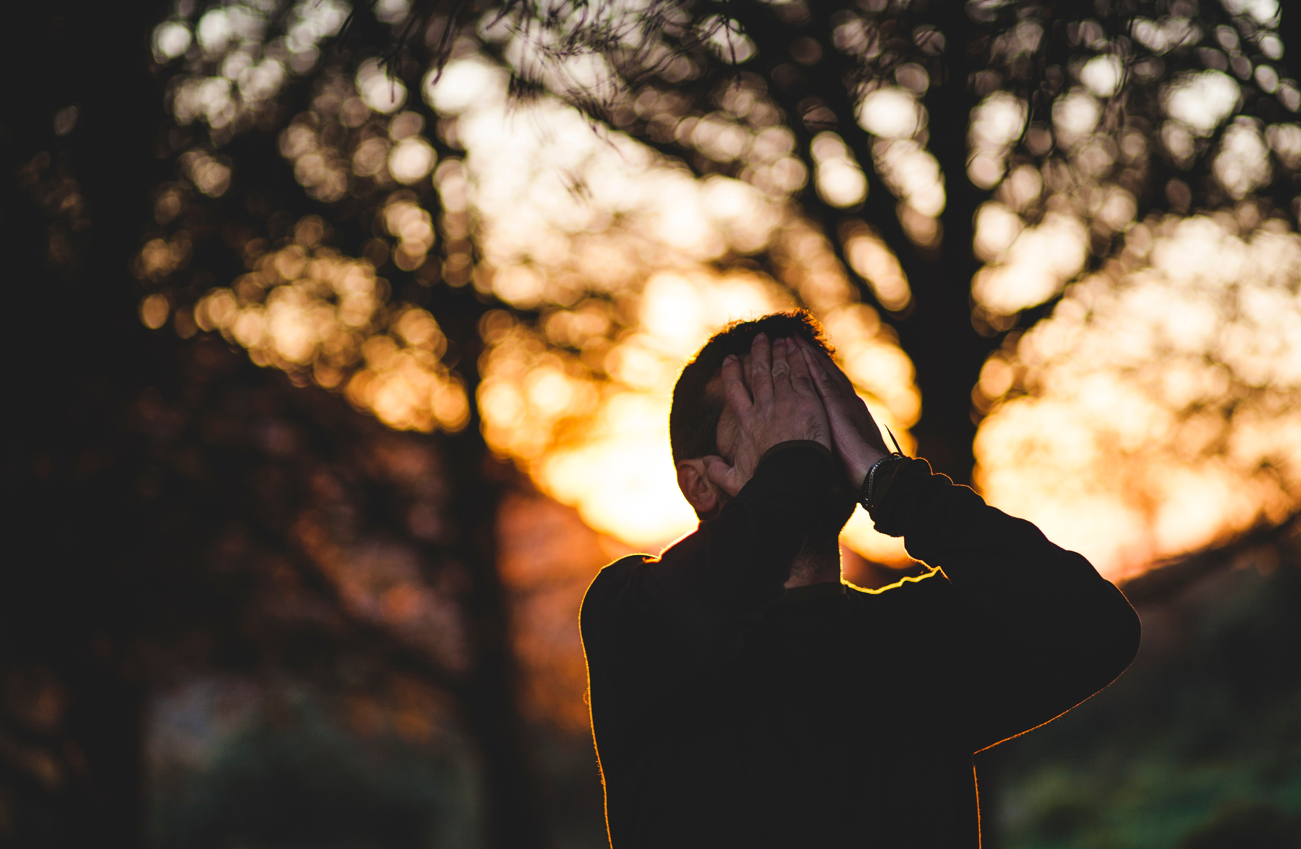 Image of a male, holding his face with his eyes closed in a forest.